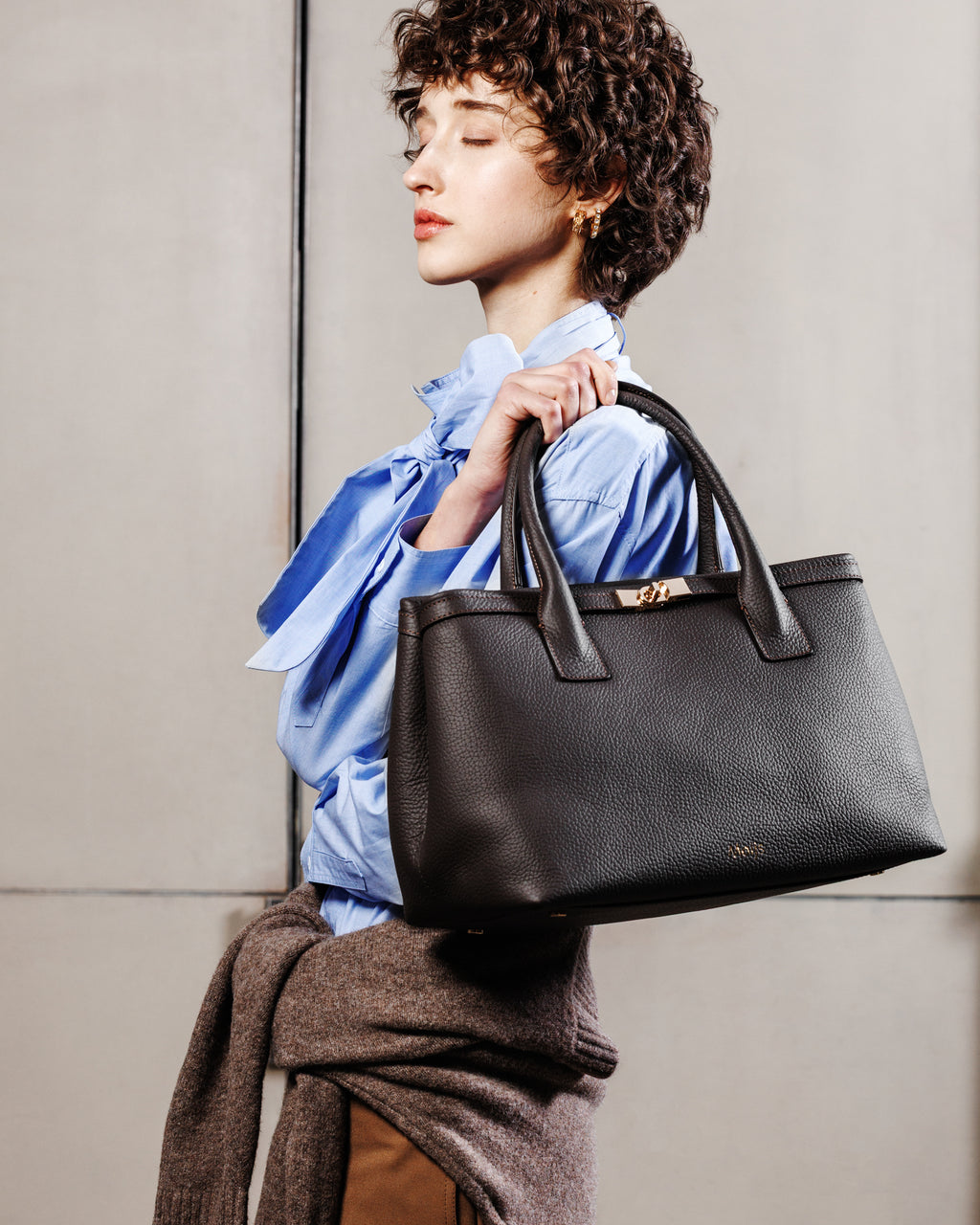 Borsa Khaite marrone Moijs indossata a spalla da modella con camicia azzurra